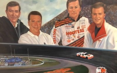 Vintage racing team photo featuring NASCAR driver Steve D. deGuzman in a Hooters-sponsored racing suit, surrounded by team members with a race car on a track backdrop, highlighting motorsports success and racing history.