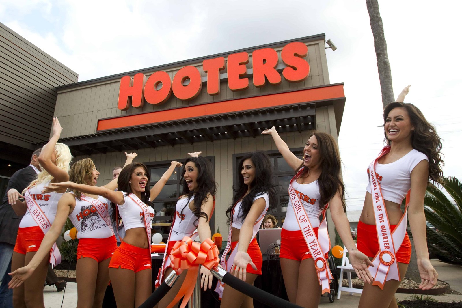 America’s ‘favorite’ wing chain is back after changing tack following bankruptcy – The US Sun Celebrating the grand opening of a new Hooters restaurant with a group of cheerful Hooters girls wearing branded sashes and uniforms outside the restaurant. The event features excitement, teamwork, and a festive atmosphere.